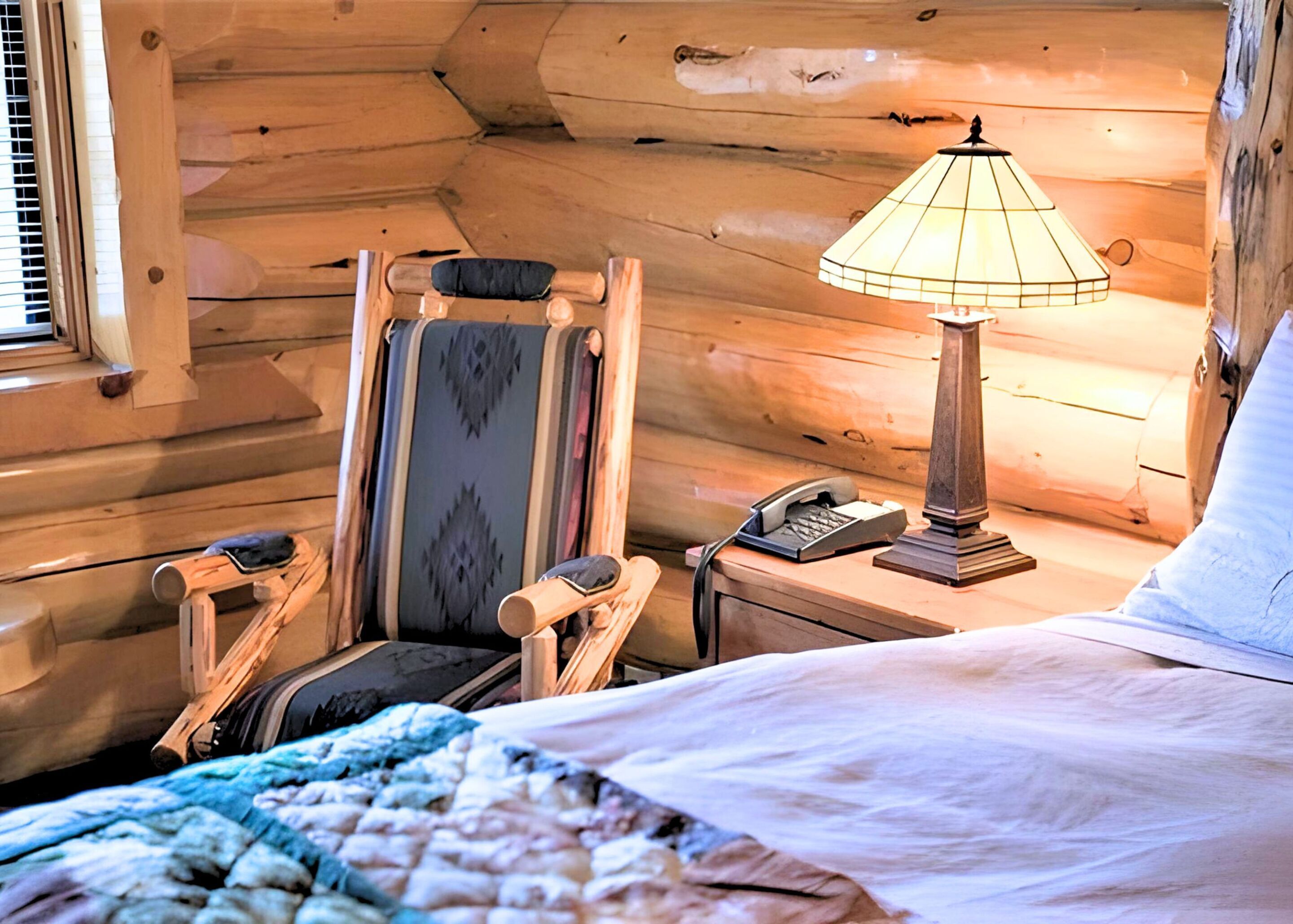 A cozy cabin room with a bed, a chair, a desk with a lamp, and a telephone.