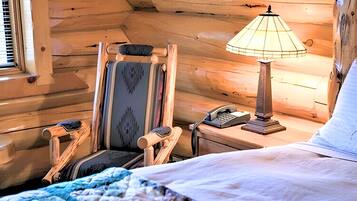 A cozy cabin room with a bed, a chair, a desk with a lamp, and a telephone.