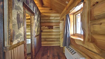 L’intérieur d’une cabane en rondins, avec des murs en bois, un plancher en bois, une fenêtre avec des rideaux et un radiateur.