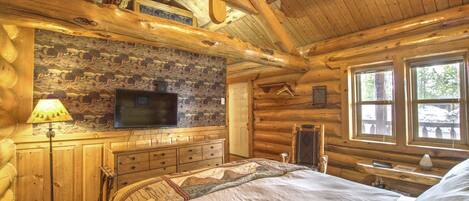 Ein Schlafzimmer in einer Blockhütte mit Bett, Kommode, Fernseher und Fenstern.