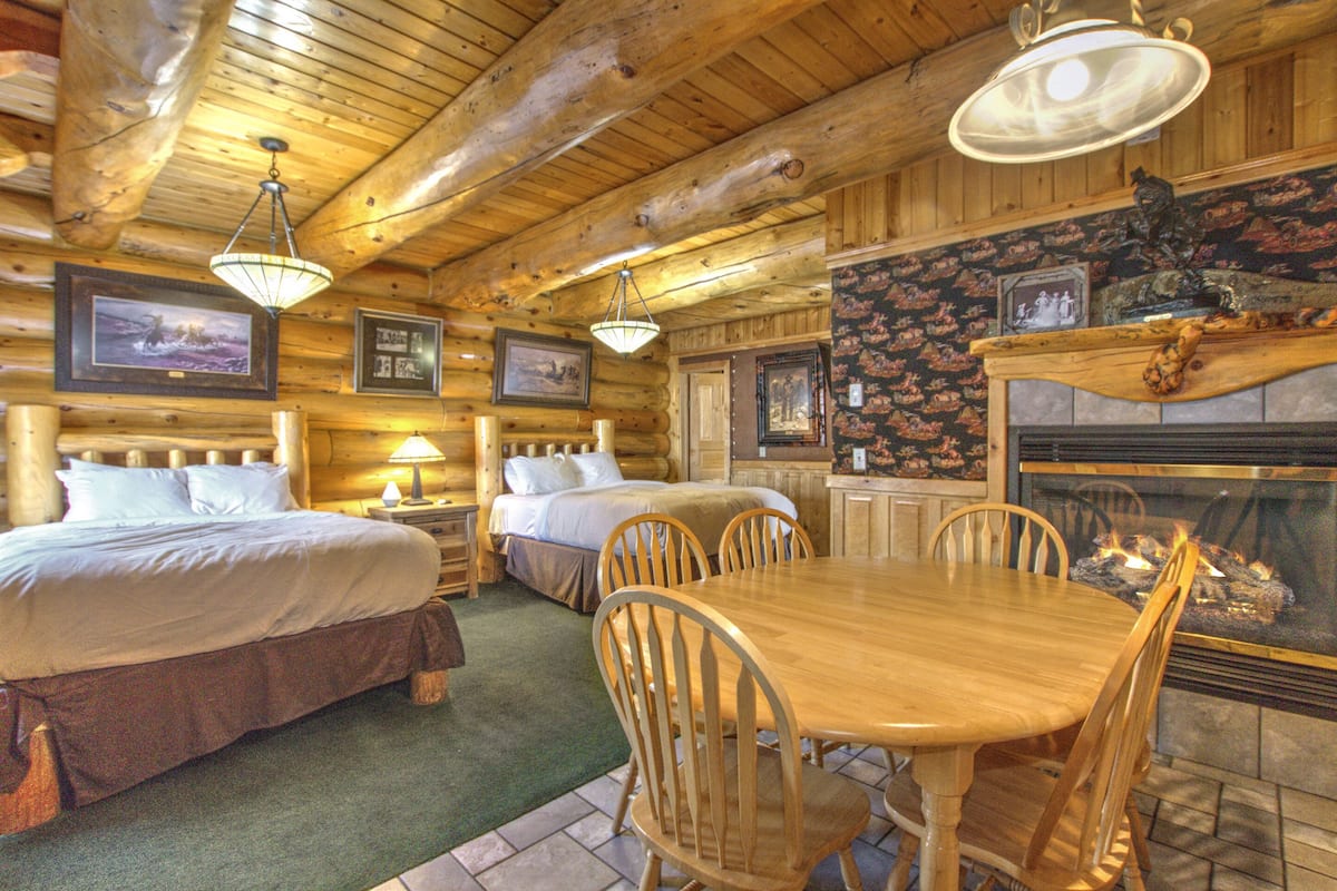 Une pièce aménagée dans le style d’un chalet en rondins, avec deux lits, une table à manger et une cheminée.