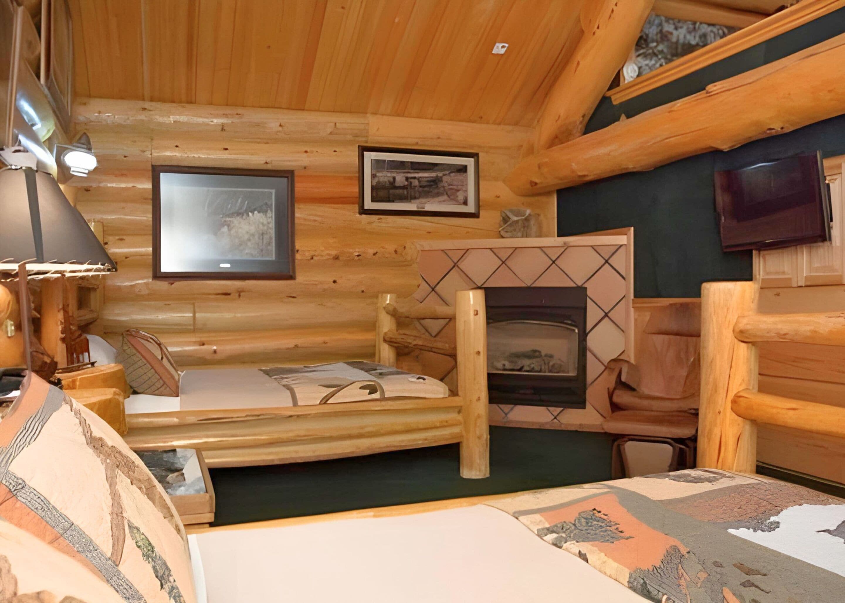 A log cabin room with a bed, a fireplace, and two framed pictures on the wall.