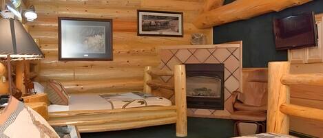 A log cabin room with a bed, a fireplace, and two framed pictures on the wall.