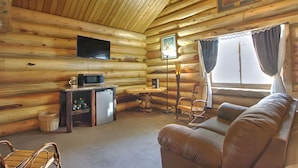 L’intérieur d’une cabane en rondins, avec un canapé, un téléviseur, un petit réfrigérateur et une fenêtre avec des rideaux.