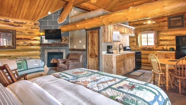 L’intérieur d’une cabane en rondins comprend un grand lit, une cheminée, une table à manger en bois et un coin cuisine.