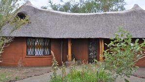 Et traditionelt stråtækt hus med en trædør og et vinduesgitter, omgivet af frodig vegetation.