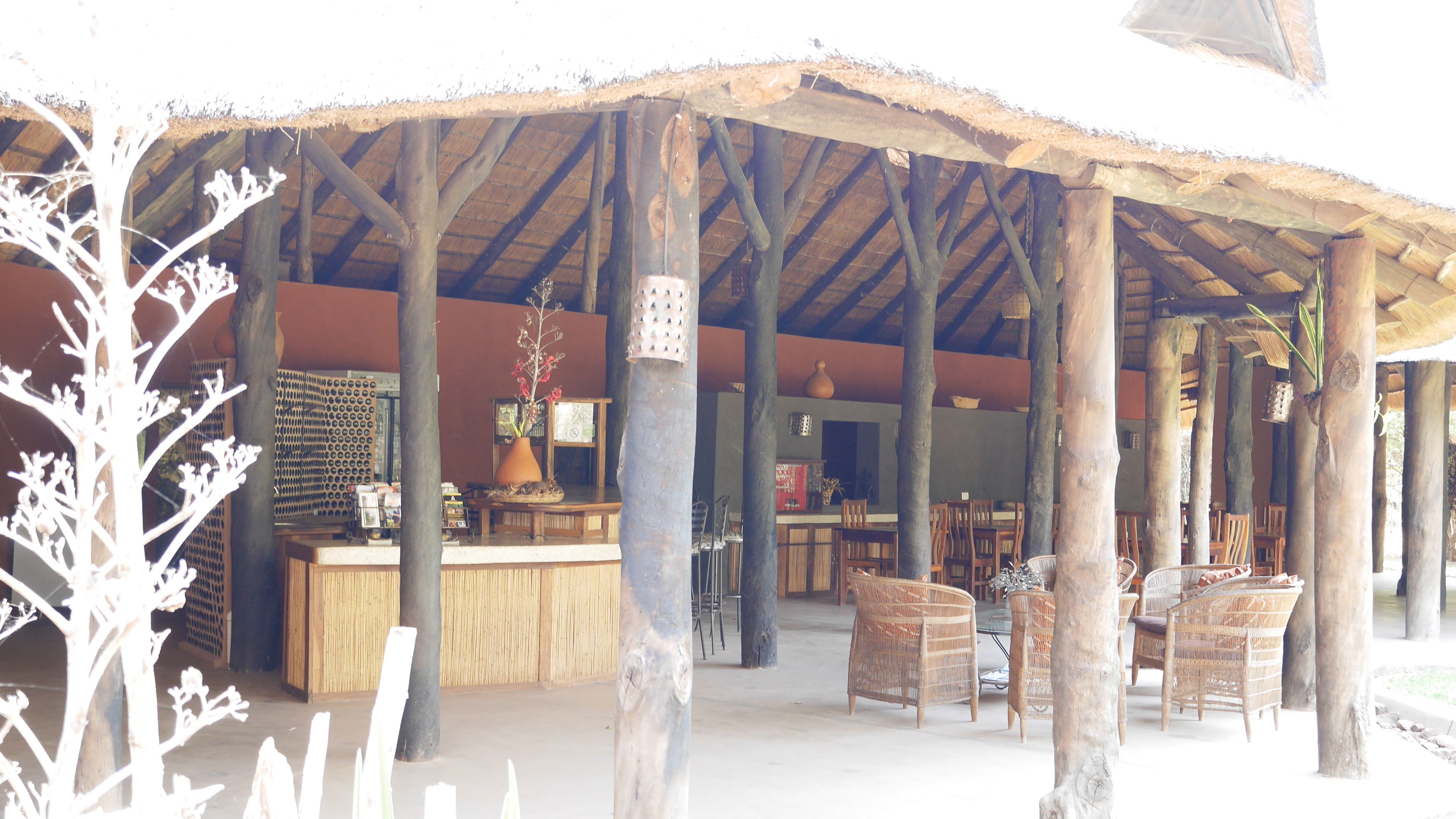 A covered outdoor seating area with wooden furniture and a thatched roof.