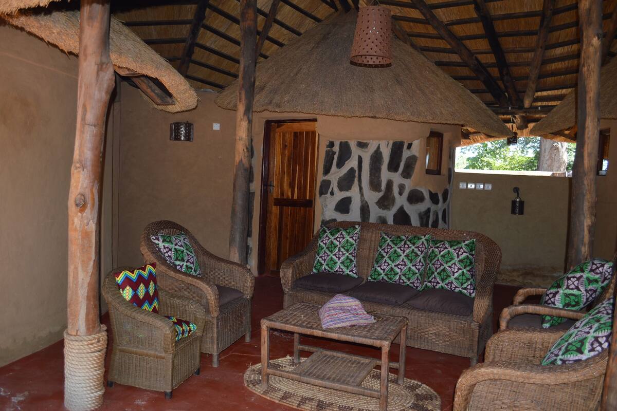 A traditional thatched-roof hut with wicker furniture and a stone wall.