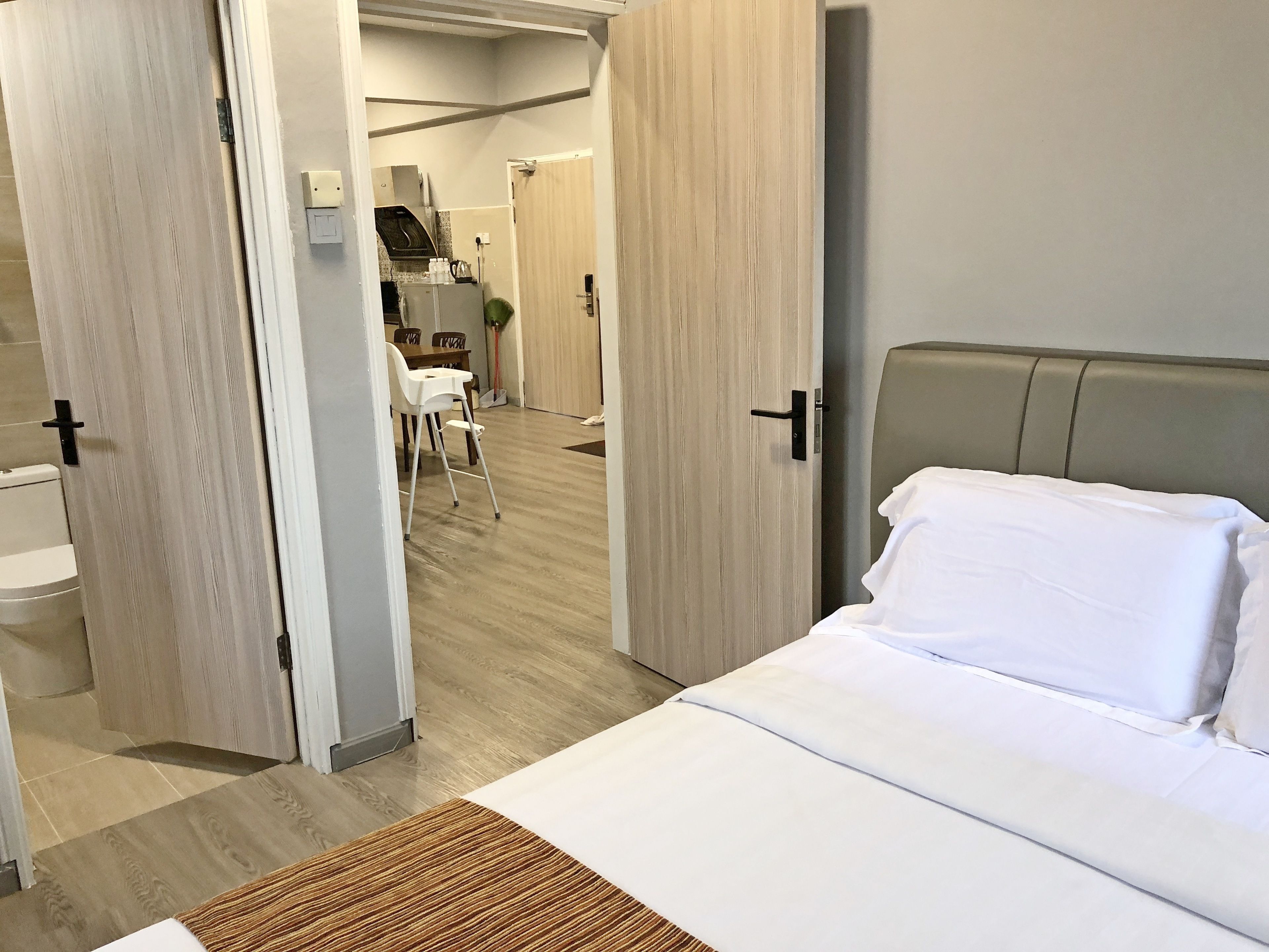 A hotel room with a bed, a wooden floor, and a view of the bathroom and dining area.