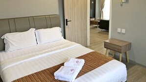 A neatly made bed with white linens and a brown striped blanket, a wooden bedside table, and a door leading to another room. - Seaview Apartment (Langkawi)