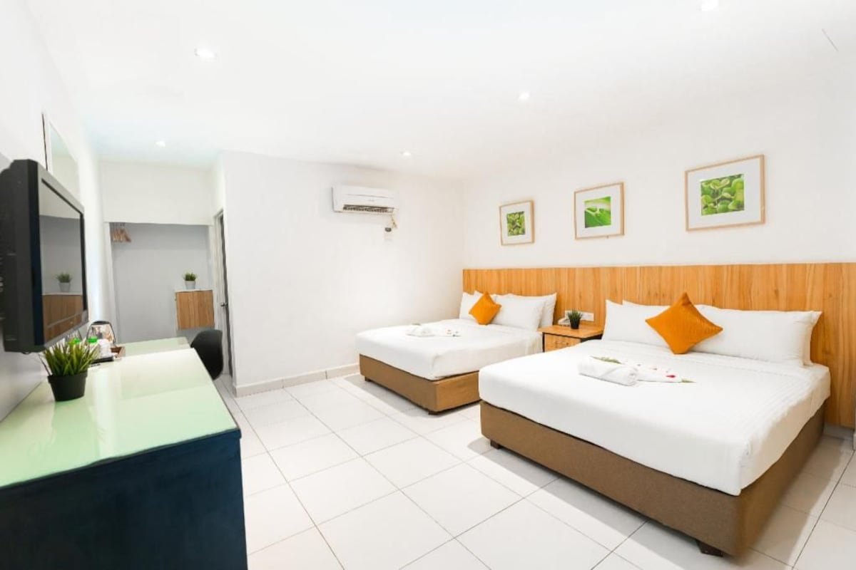 A hotel room with two beds, a desk, a TV, and a wall-mounted air conditioner.