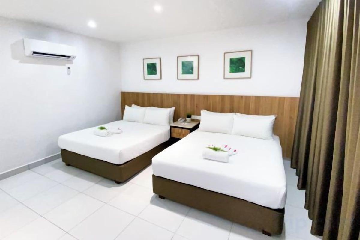 A hotel room with two beds, a wooden headboard, a nightstand, and an air conditioning unit.