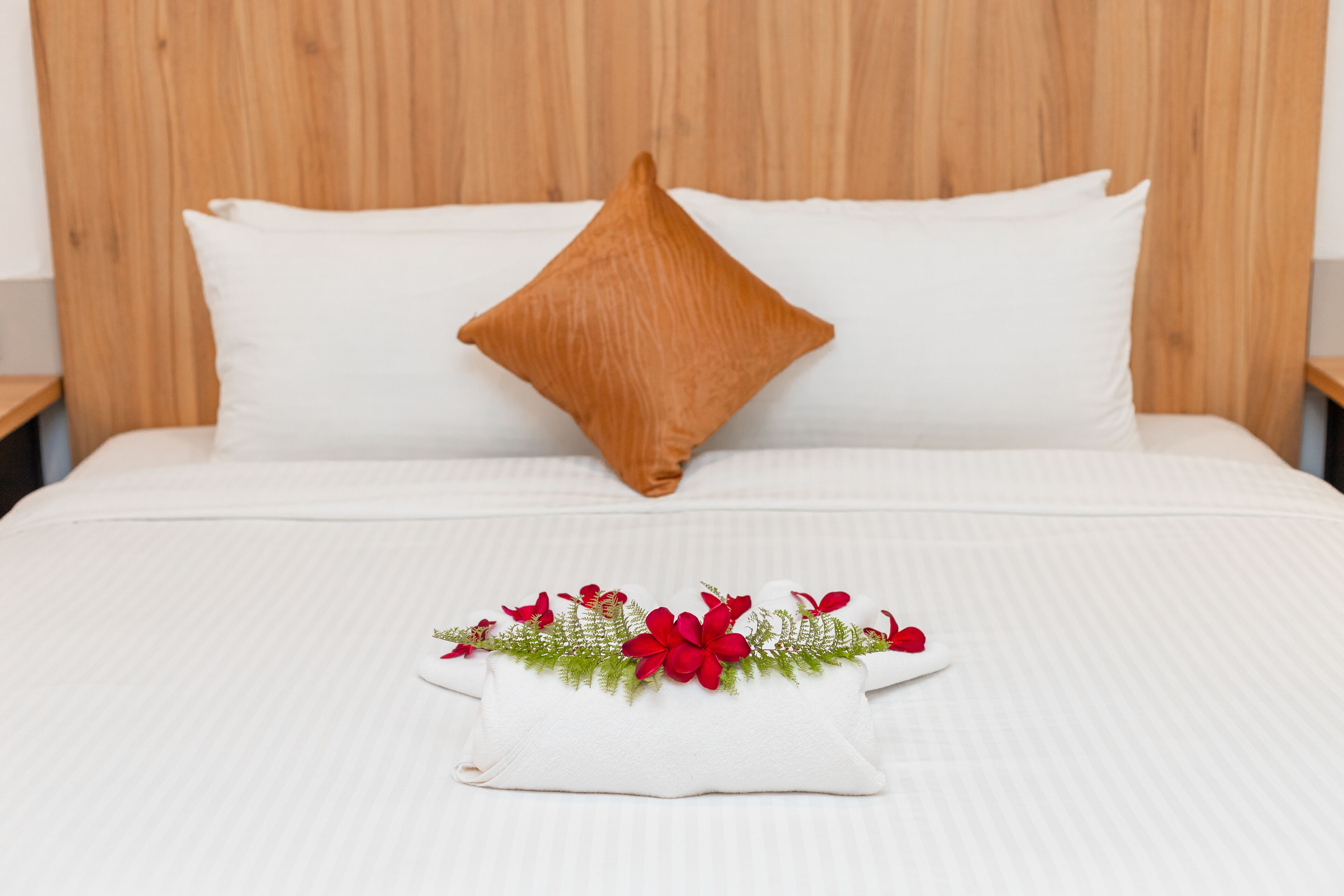 A bed with white bedding, a brown pillow, and a decorative pillow with red flowers and green foliage.