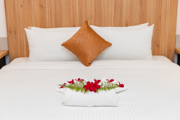 Una cama con ropa de cama blanca, un almohadón marrón y un cojín decorativo con flores rojas y follaje verde.