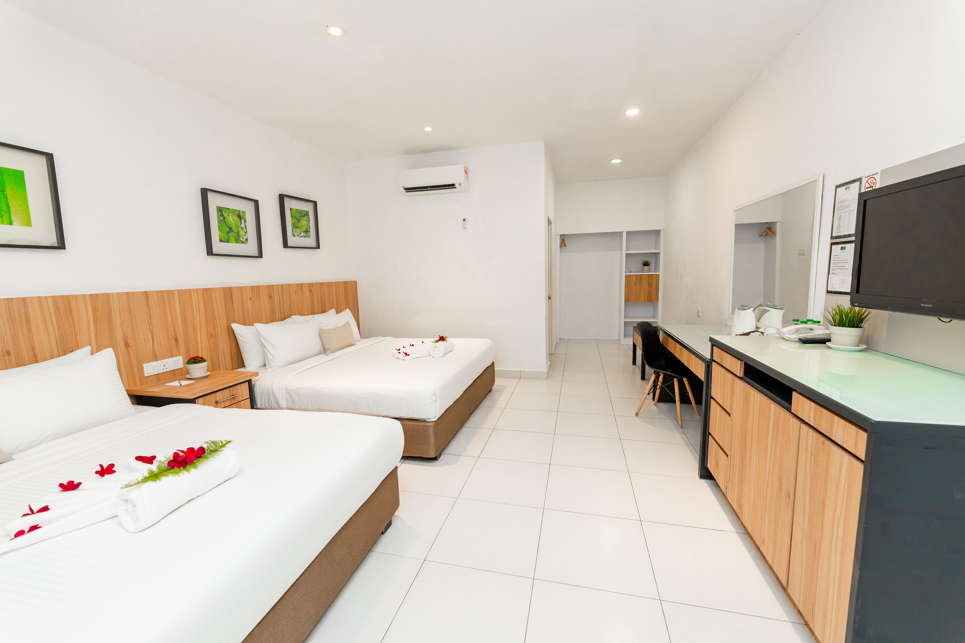 A modern hotel room with two beds, a desk, a TV, and a bathroom visible through an open door.