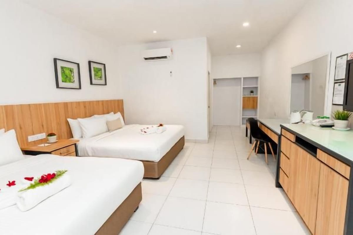 A hotel room with two beds, a kitchenette, a TV, and a bathroom visible in the background.