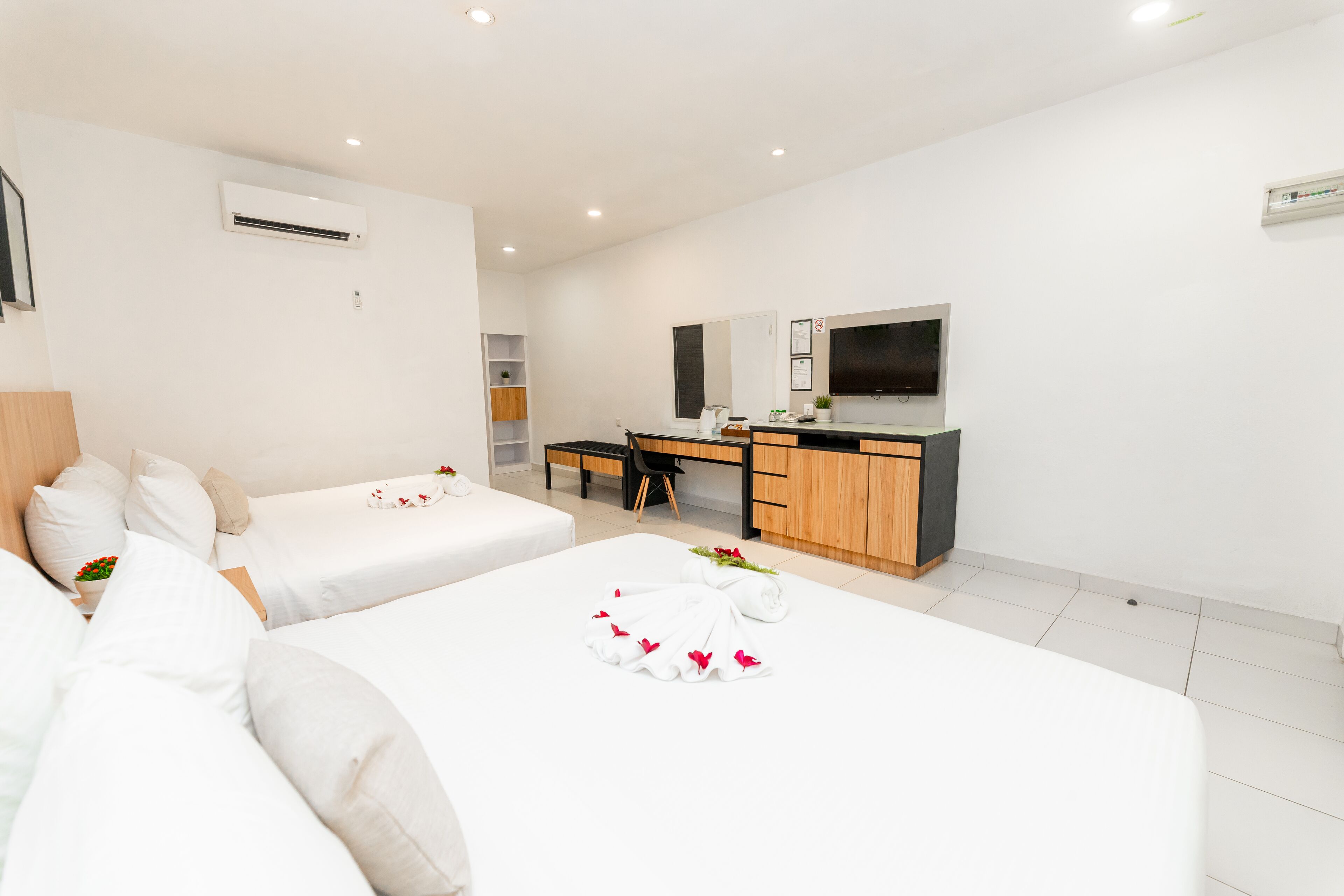 A hotel room with two beds, a desk, a TV, and an air conditioning unit.