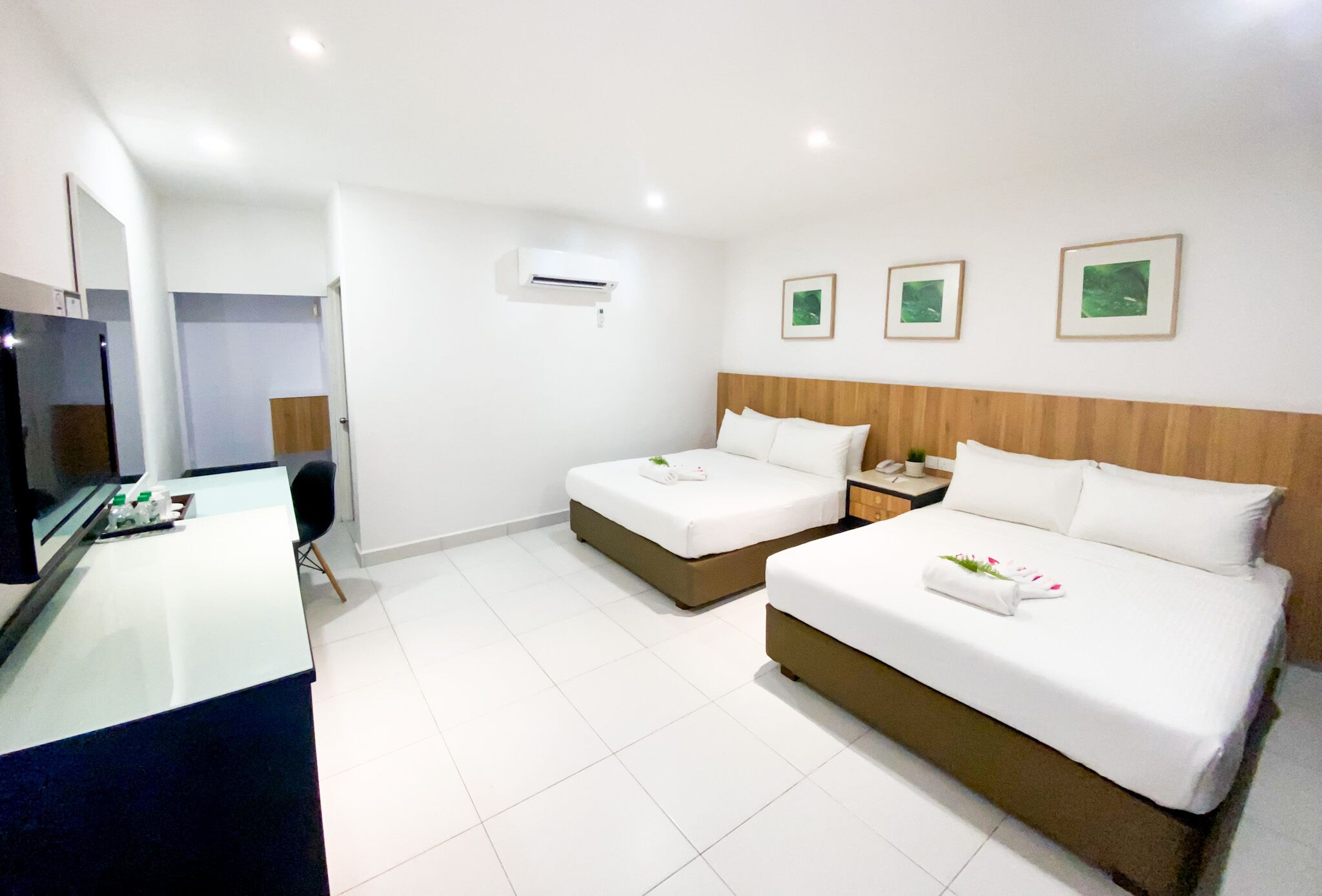 Ein Hotelzimmer mit Schreibtisch, zwei Betten, einem Holz-Kopfteil und drei gerahmten Bildern an der Wand.