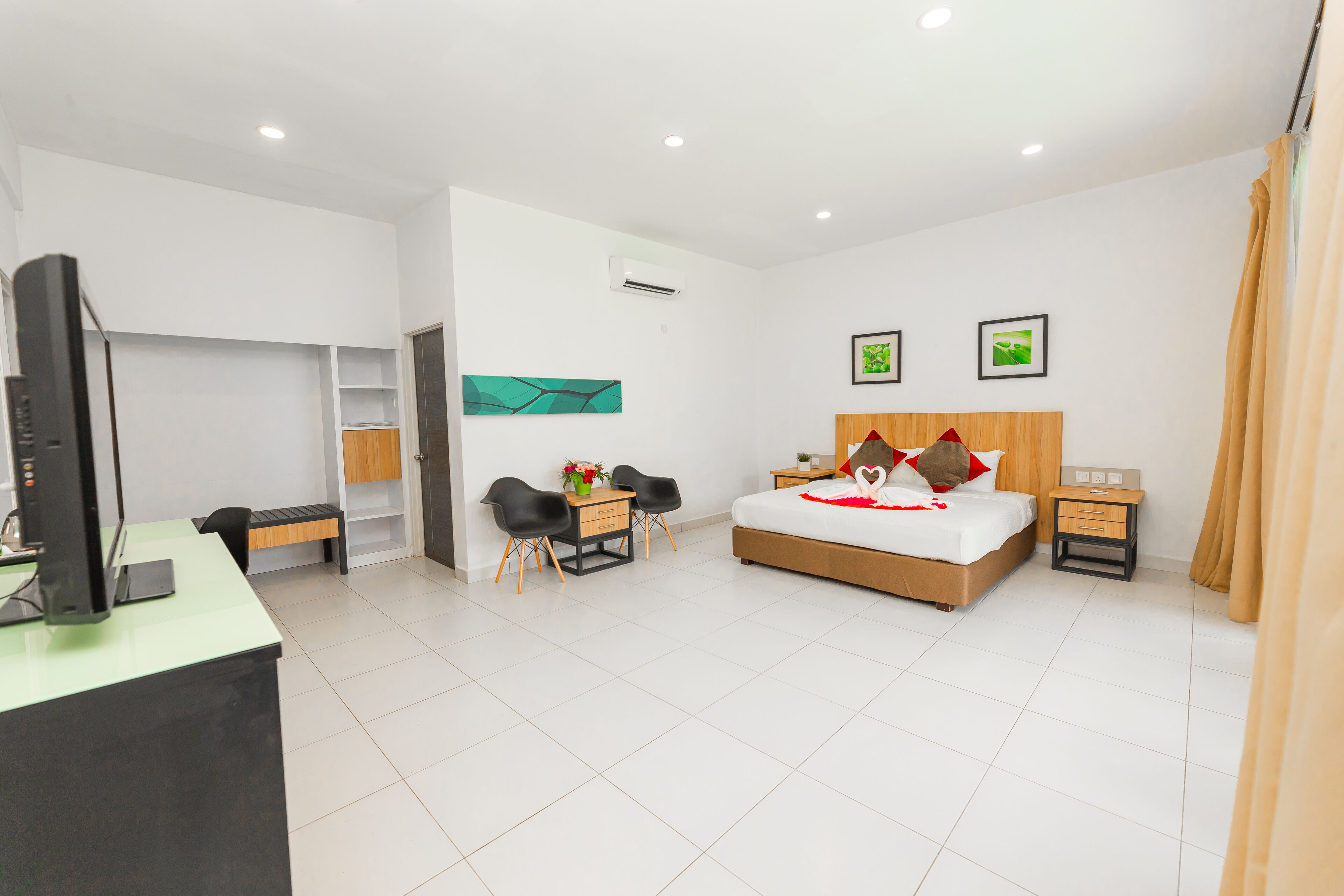 A modern hotel room with a bed, desk, chairs, and a TV.