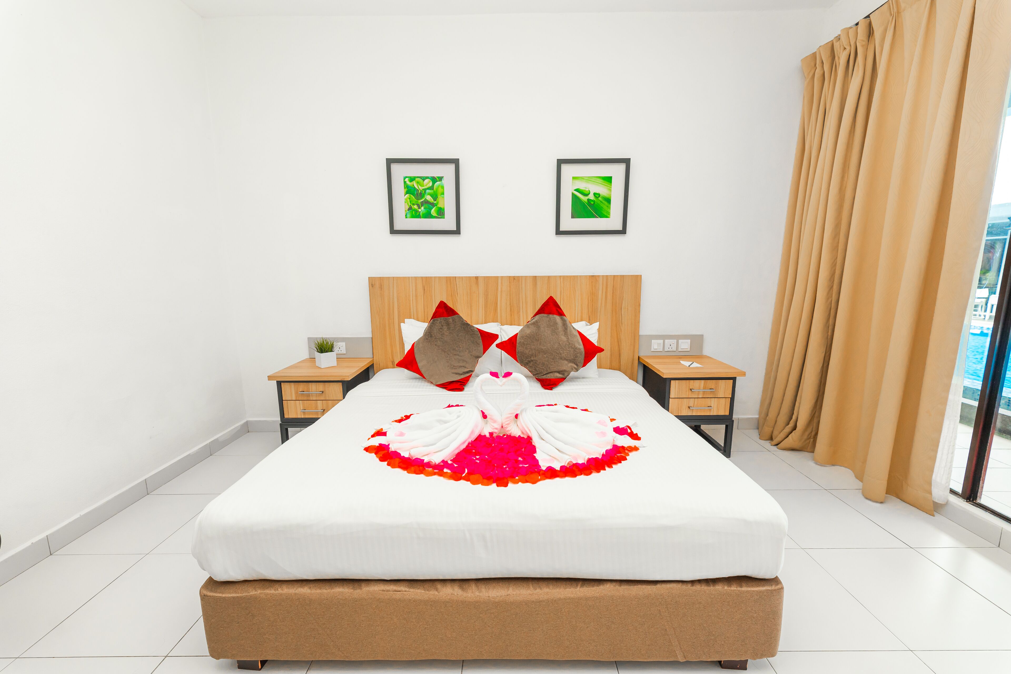 Une chambre d’hôtel avec un grand lit, deux tableaux encadrés au mur, une table de chevet avec une lampe et une fenêtre avec des rideaux.
