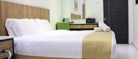 A hotel room with a bed, a bedside table, a mirror, a dresser, and a door.