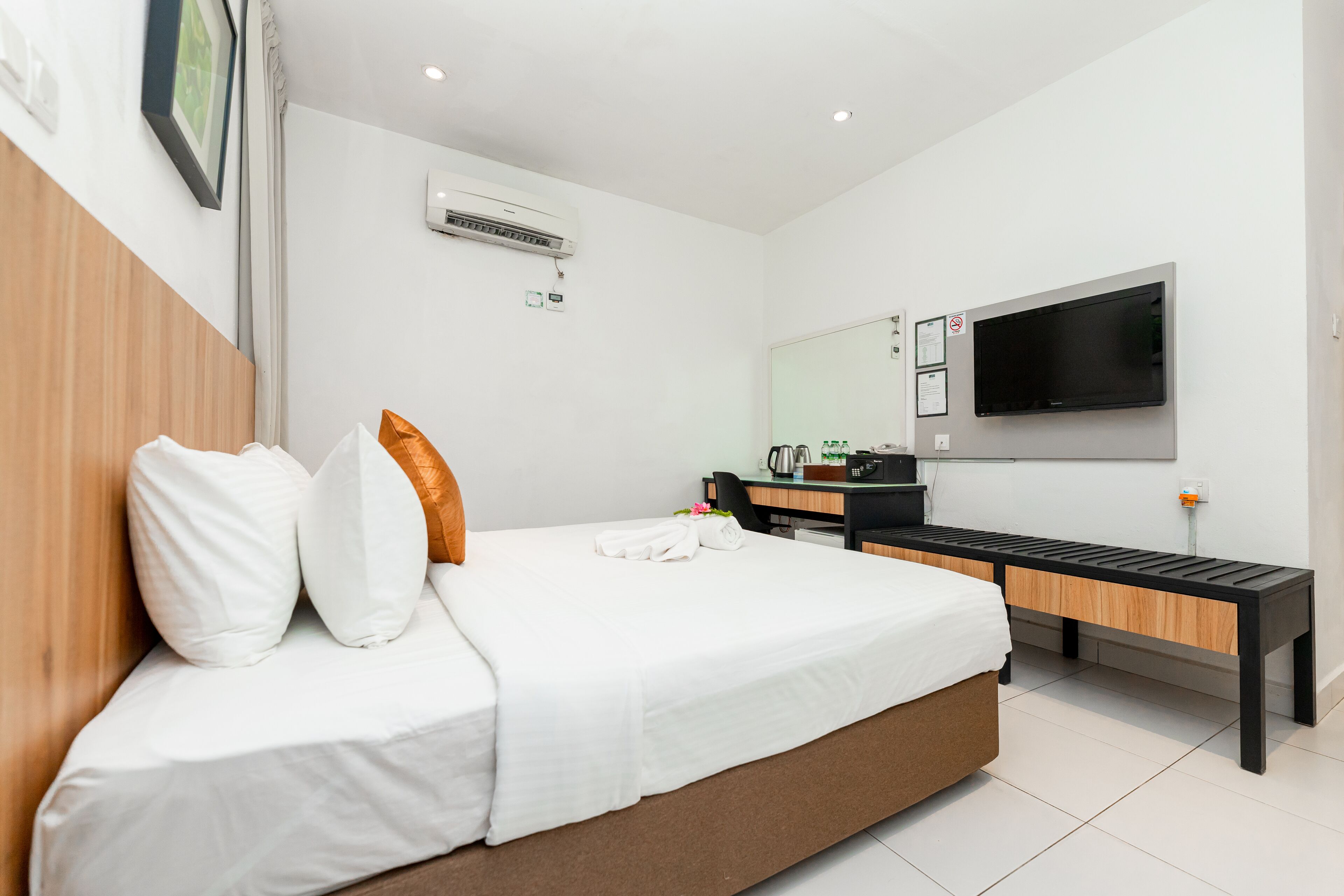 A modern hotel room with a large bed, a desk, a chair, a flat-screen TV, and an air conditioning unit.