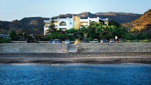 Et kysthotel med flere balkoner, en swimmingpool og udsigt til havet og bakker.