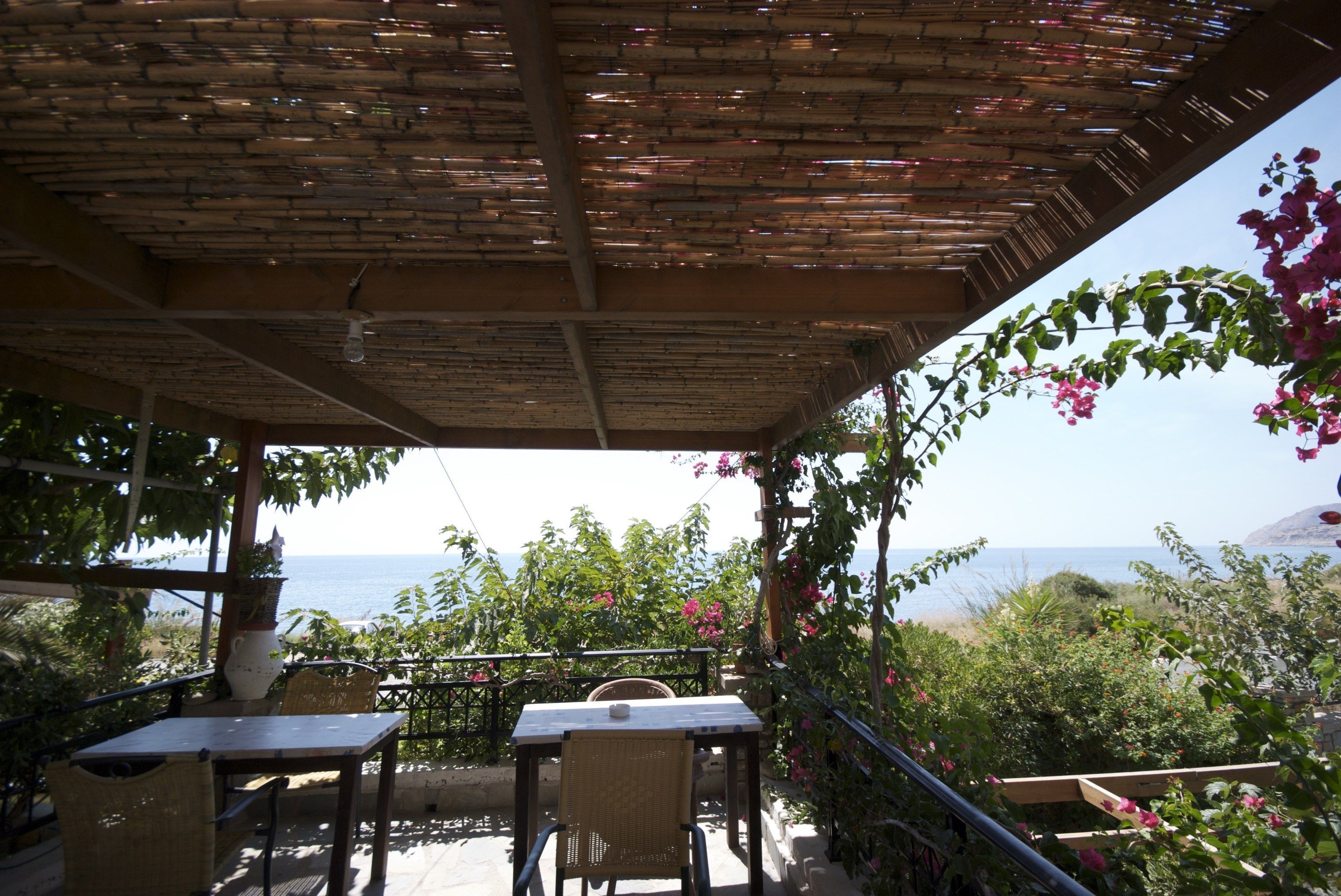 An outdoor patio with a table and chairs, a pergola overhead, and a view of the sea.
