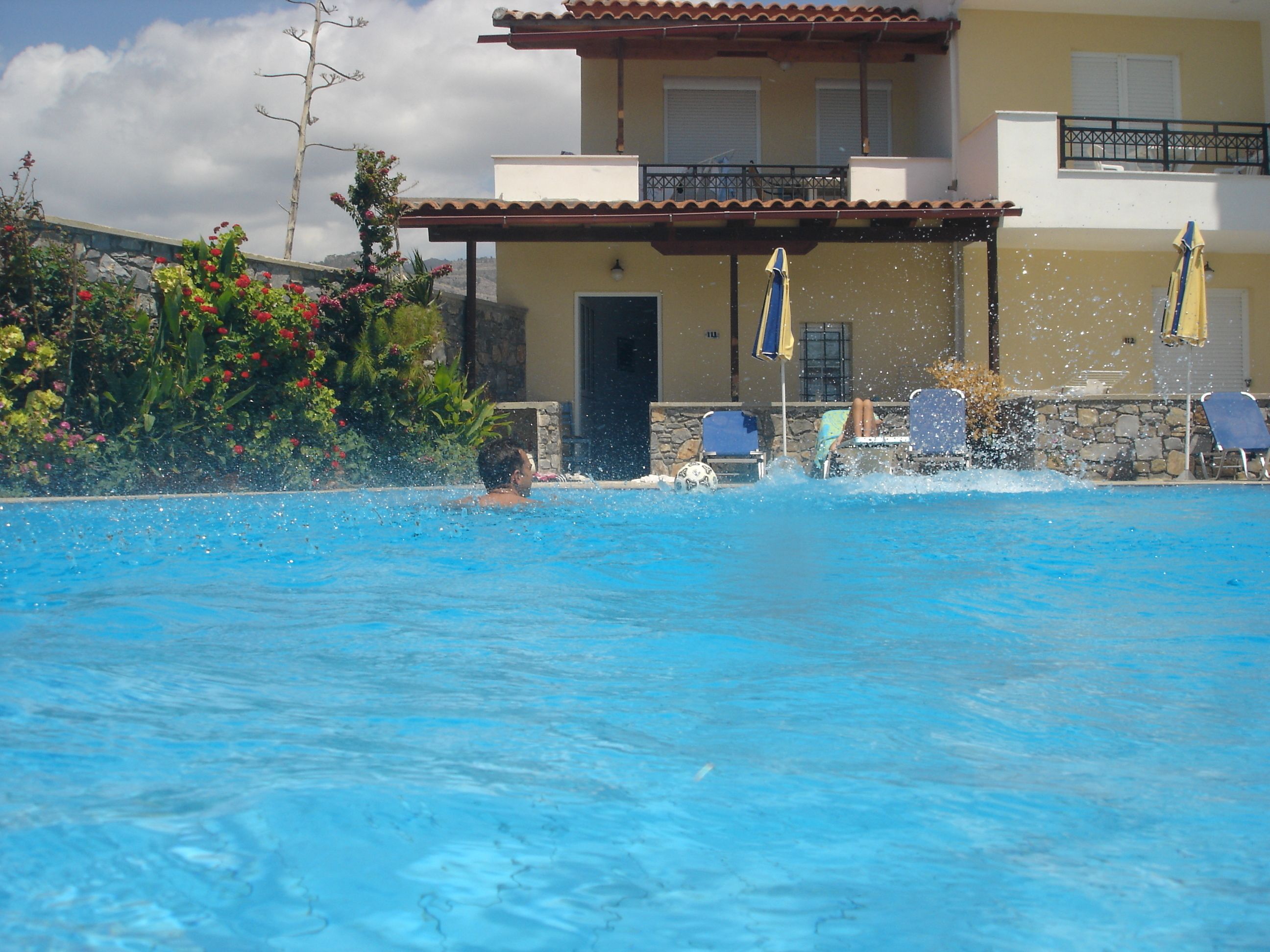 A swimming pool with a person swimming, surrounded by lounge chairs and umbrellas.