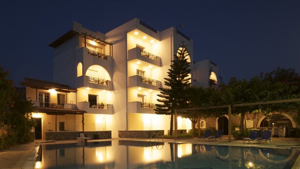En moderne bygning med swimmingpool, flere balkoner og en veloplyst facade.