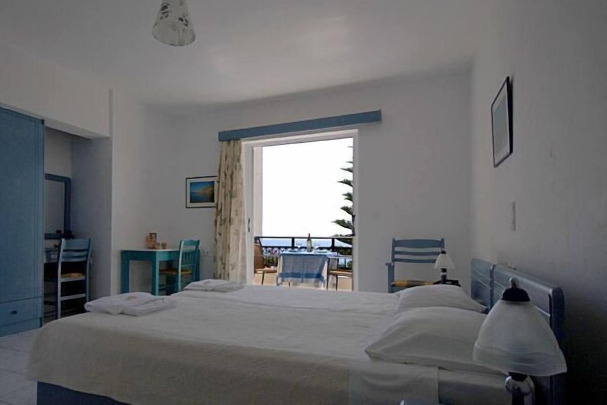 A bedroom with a bed, a desk, a chair, and a balcony with a view.