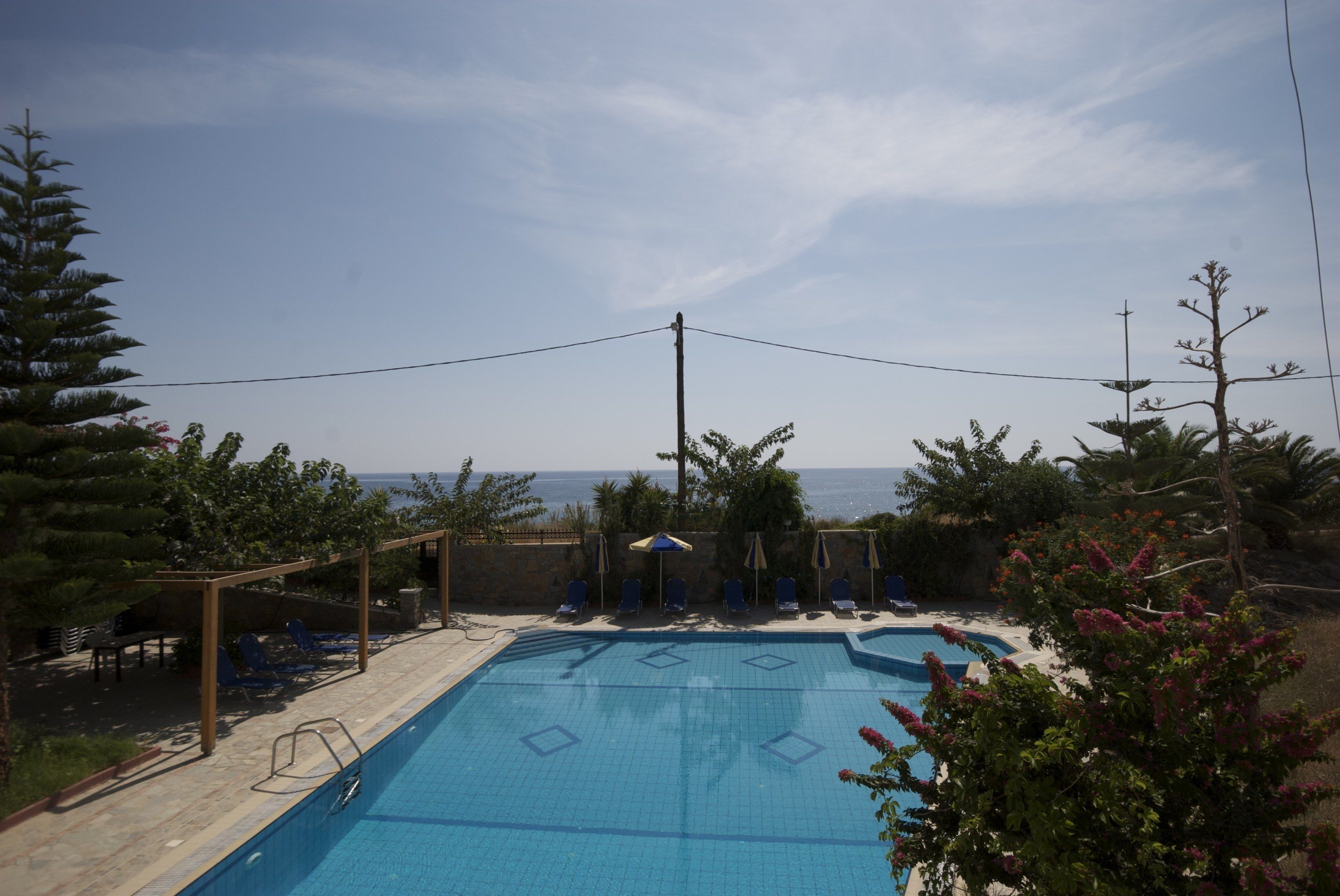 A swimming pool with lounge chairs and umbrellas, surrounded by trees and overlooking a body of water.