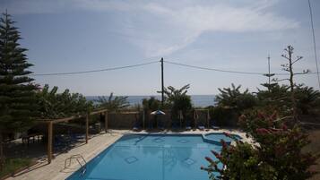A swimming pool with lounge chairs and umbrellas, surrounded by trees and overlooking a body of water.
