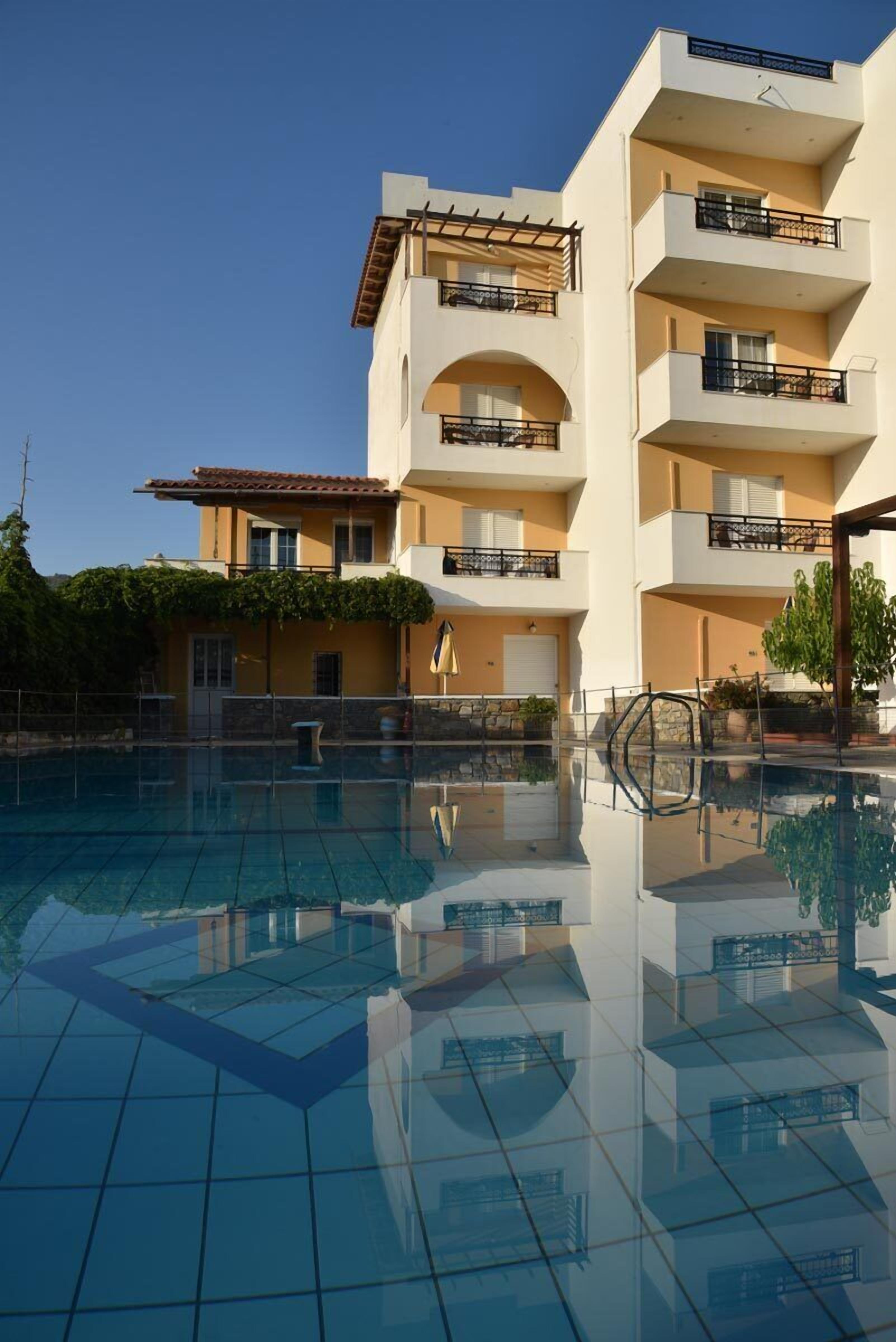 A multi-story hotel with a swimming pool, balconies, and a clear sky.