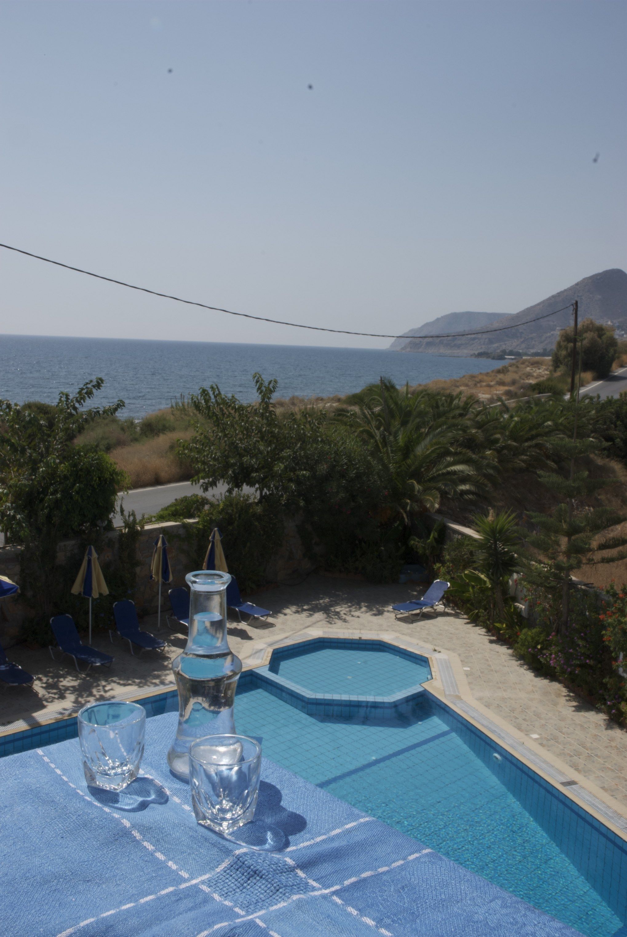 A pool area with lounge chairs and a table, overlooking a coastal landscape with a mountain in the distance.