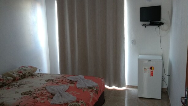 Un dormitorio con cama, cortinas, televisor y refrigerador.