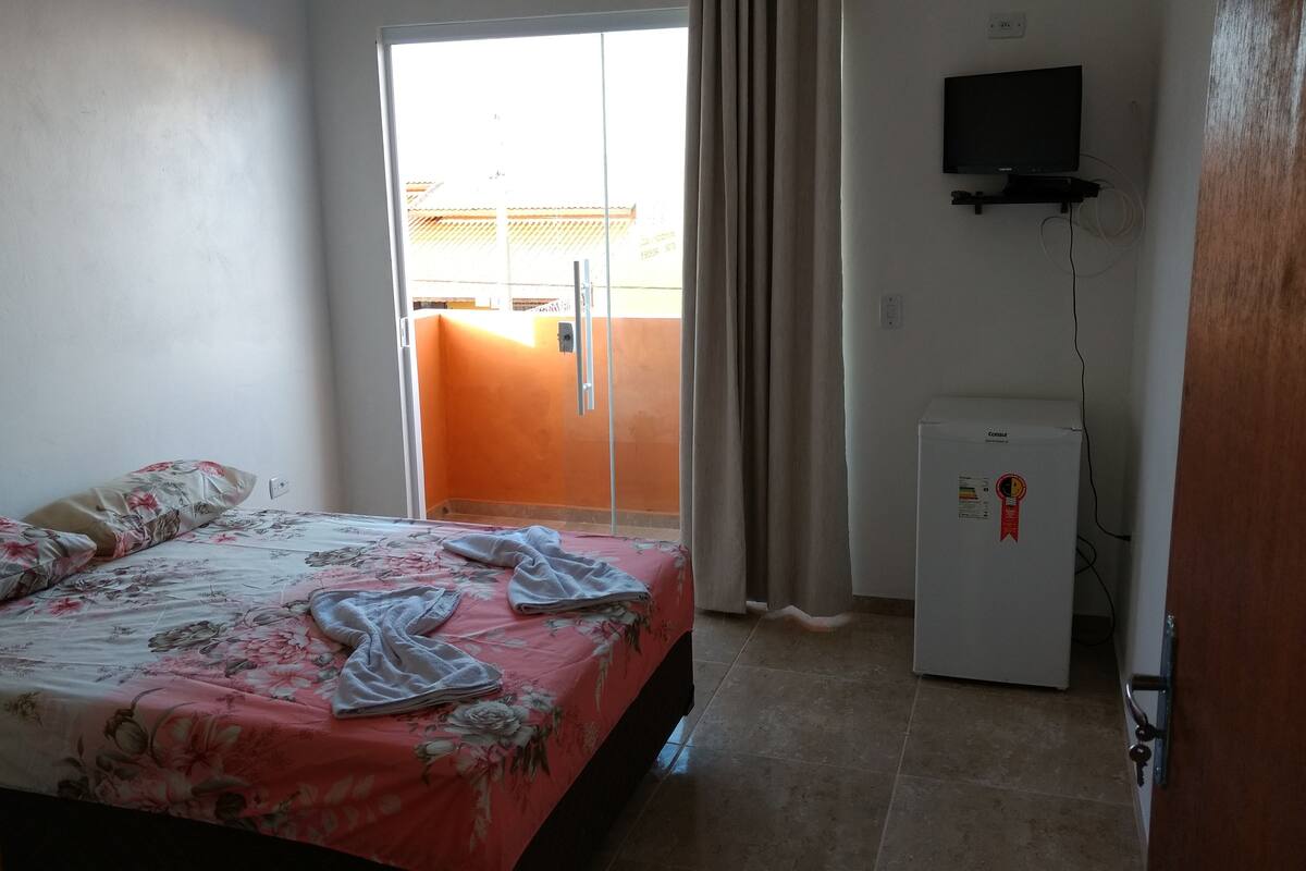 Quarto com cama, televisão e frigorífico.
