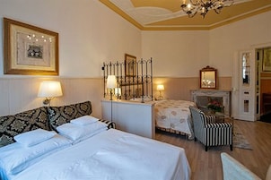 Ein Hotelzimmer mit einem großen Bett, einem kleineren Bett, einem Sessel, einem Kamin und einer Chandelier.
