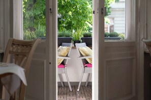 An open door leading to a patio with wicker chairs and a table, surrounded by potted plants and a view of greenery. - Hotel Augusta (Berlin)
