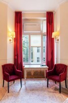 Una habitación con dos sillas rojas, una mesita y una ventana con cortinas rojas.