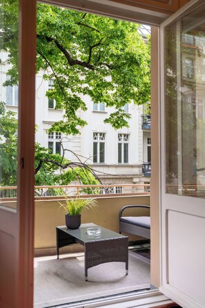 A balcony with a table, chair, potted plant, and a view of a building with windows. - Hotel Augusta (Berlin)