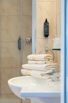 Un baño con lavamanos, toallero con toallas dobladas, ducha y una botella de champú en la pared.