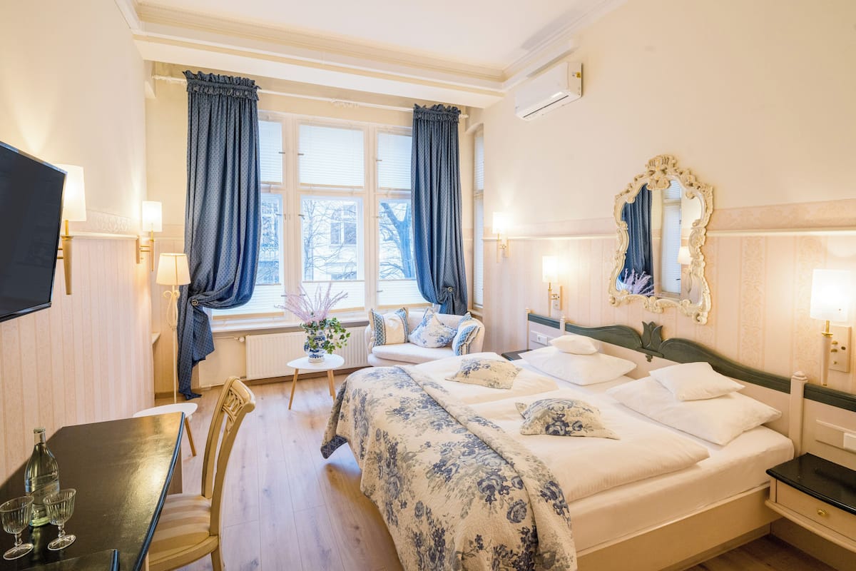 A hotel room with a bed, a desk with a chair, a TV, and a window with curtains.