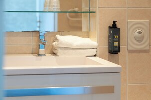 Un baño con repisa de vidrio, toalla blanca, botella negra y dispensador de jabón.