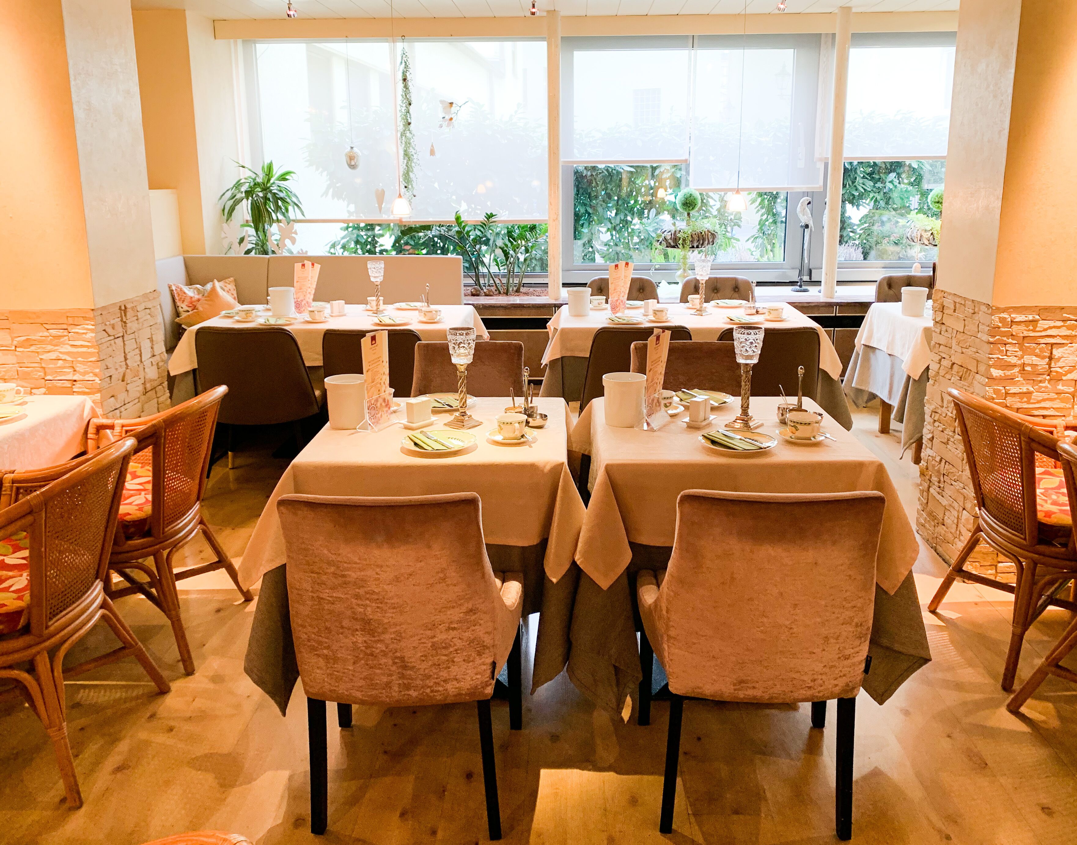Un restaurante con mesas dispuestas para comer, sillas y vistas al exterior con vegetación.