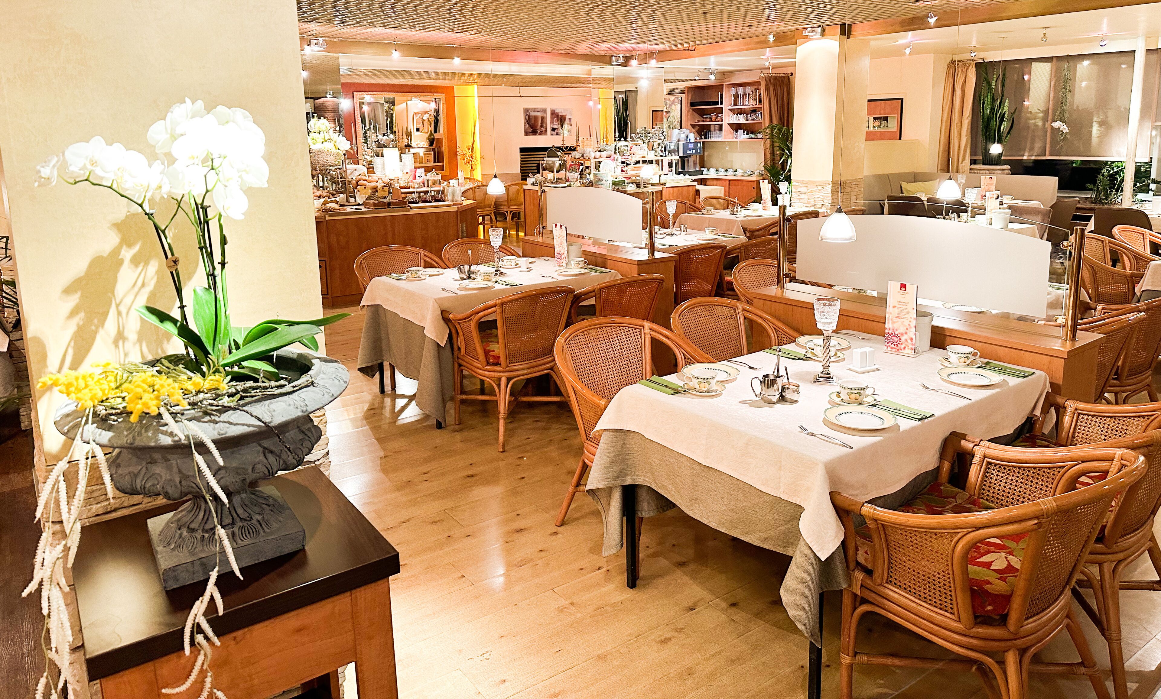 Un restaurante con varias mesas y sillas, un centro de mesa decorativo con flores y un ambiente interior cálido.