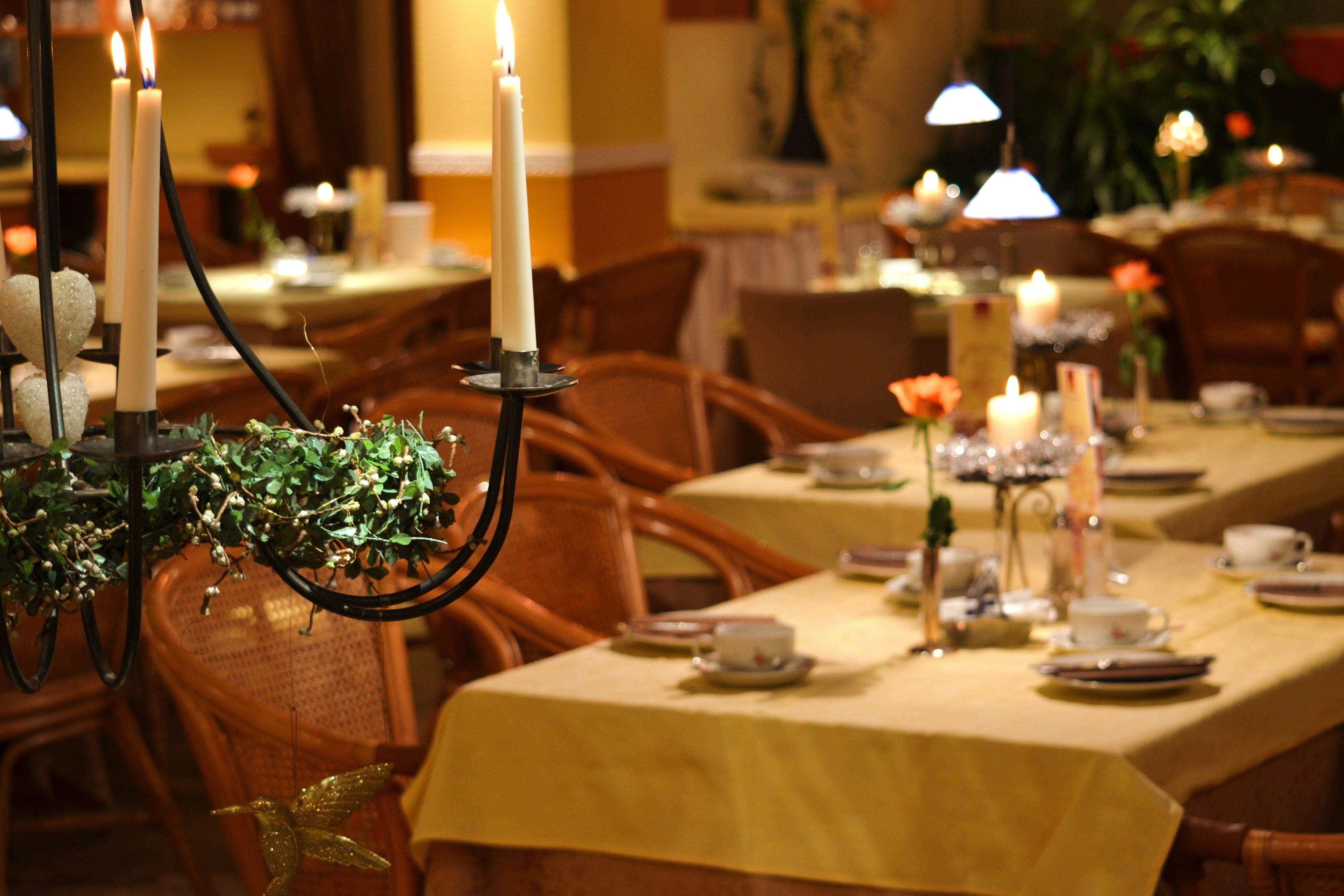 A dining area with tables set for service, candles, and a decorative plant.