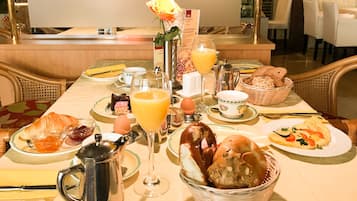Un desayuno con cruasanes, pan, una cesta de muffins, un vaso de zumo de naranja y una rosa sobre la mesa.