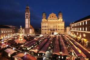 A historic building with a clock tower and a Christmas market with tents. - City Hotel Ost am Kö (Augsburg)