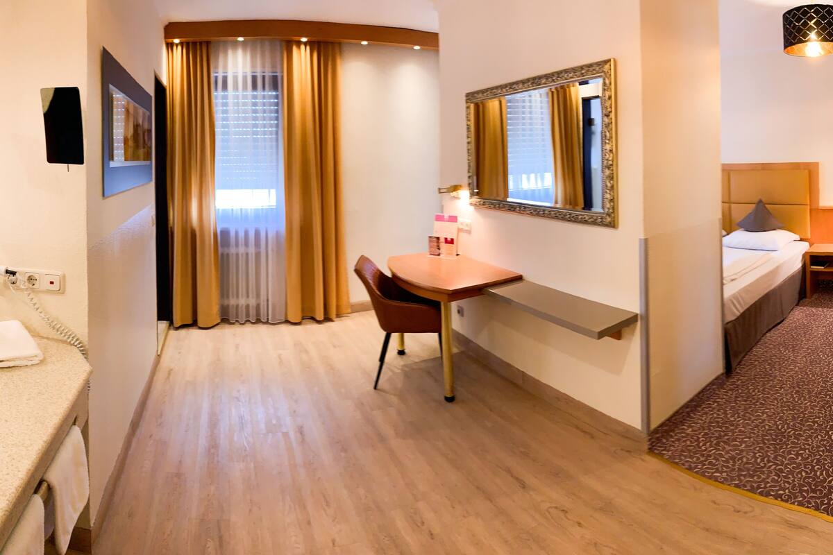A hotel room with a bathroom, a desk, a bed, and a large mirror.